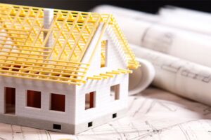 Small plastic version of a house being constructed with building plans underneath and rolled building plans to the right