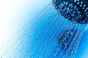 Up close of shower head with running water and blue background
