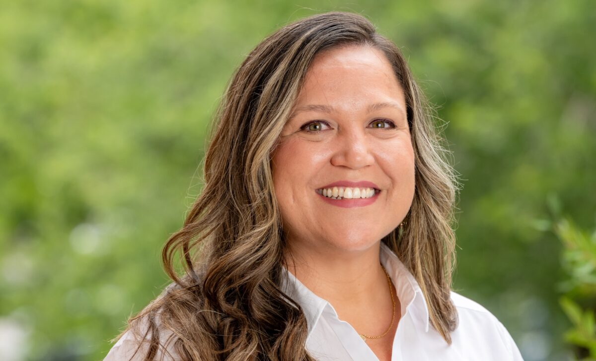 Peggy shown from shoulders up looking at camera with white shirt and green background
