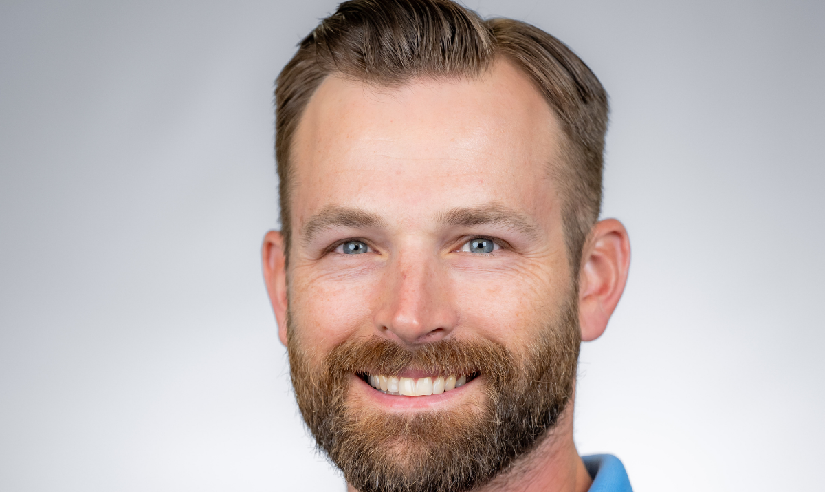 Jordan is looking at the camera and is shown from chin up with blue shirt and gray background