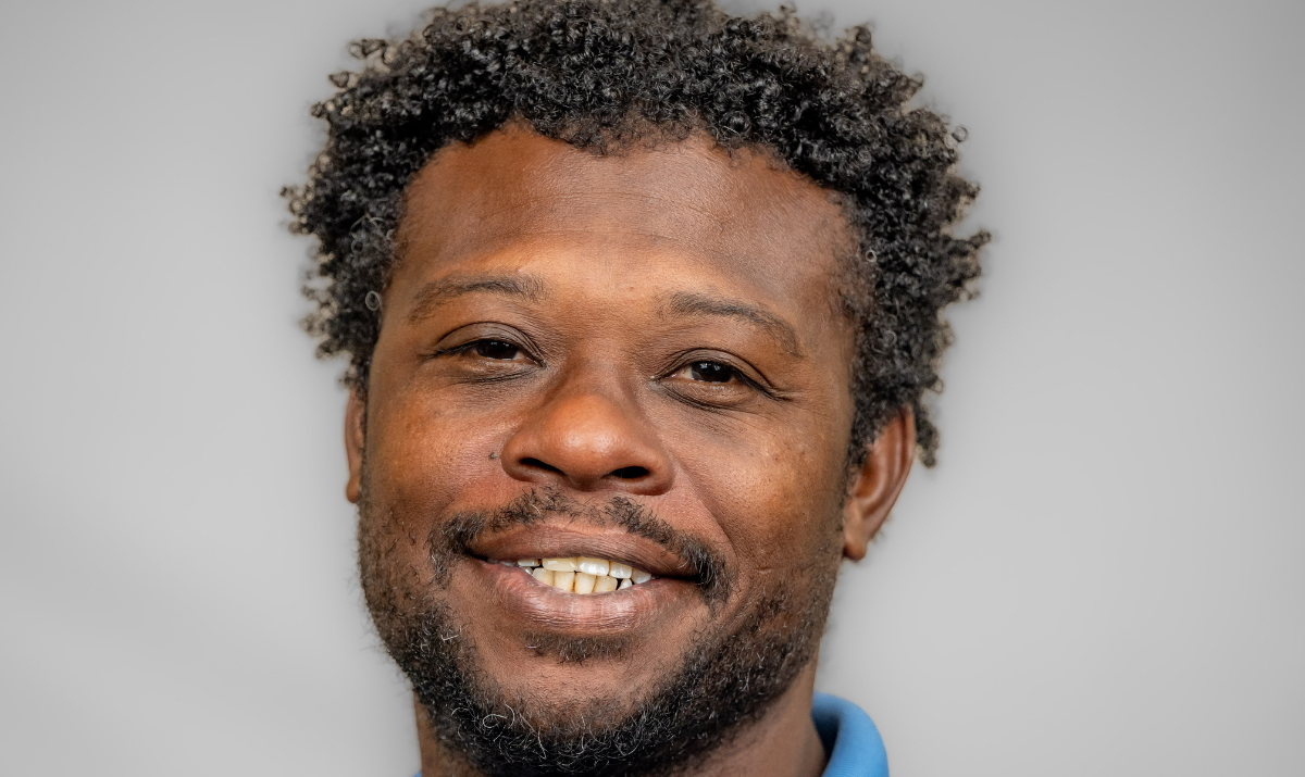 Darius looks at camera and is shown from neck up with blue shirt and gray background