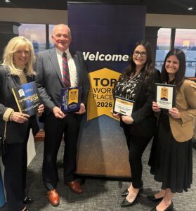 Four people stand around top workplace banner holding awards
