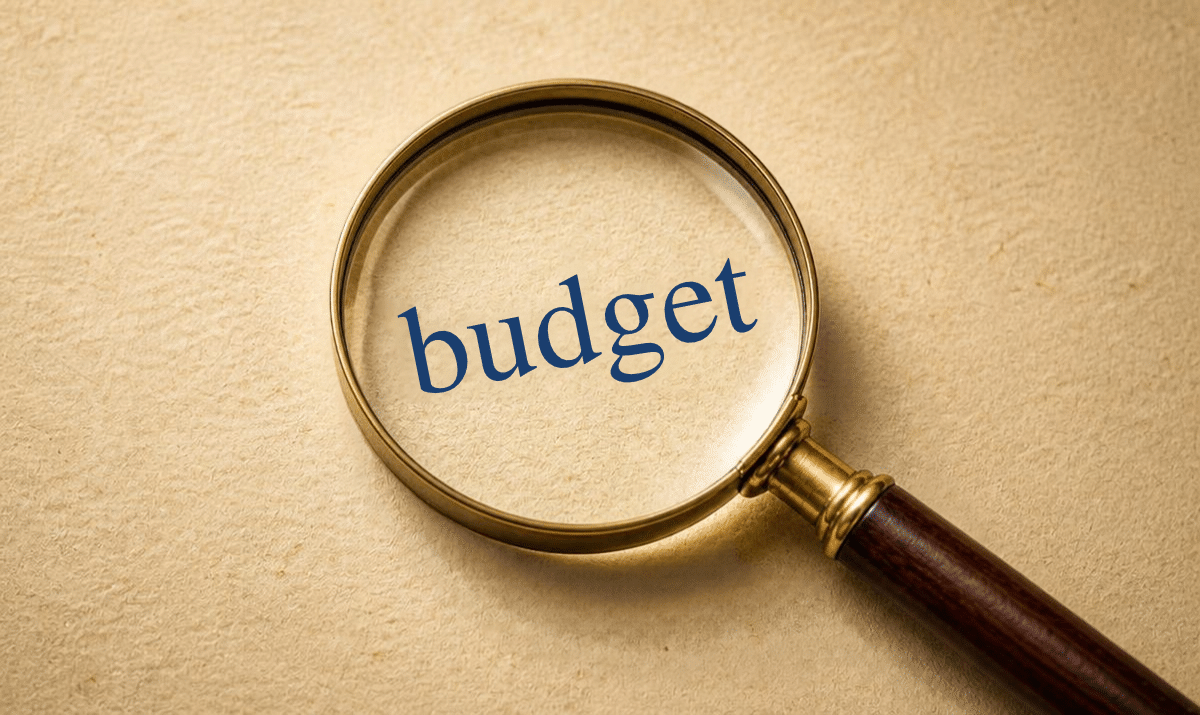 The word budget is under a magnifying glass on beige paper